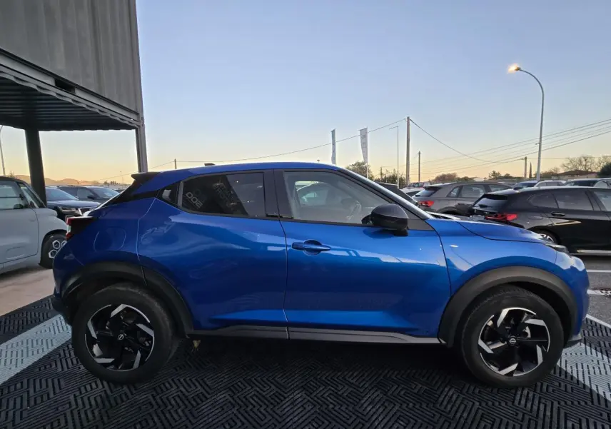 Profil côté gauche du Nissan Juke II bleu magnetic avec jantes alliage noires et toit noir visible en extérieur.