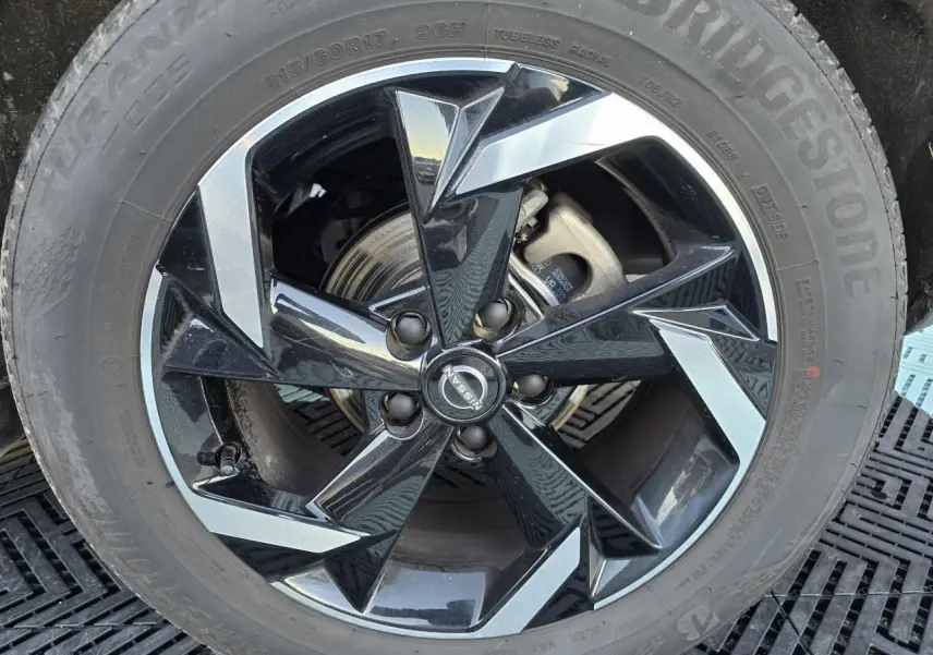 Gros plan sur la jante alliage 17 pouces noire et argentée du Nissan Juke II bleu Magnetic avec logo central Nissan.