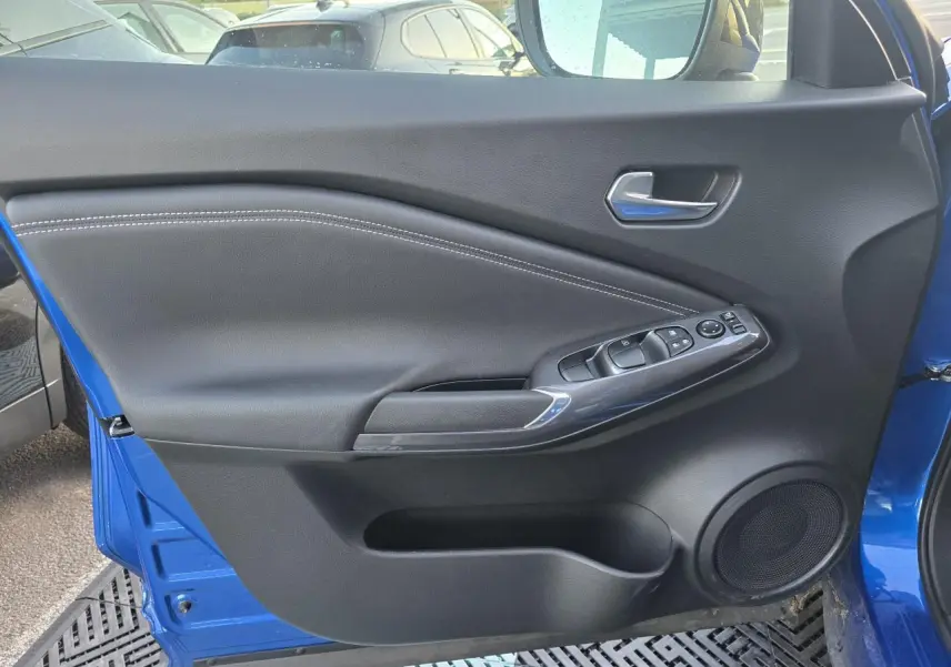 Vue côté gauche de la porte avant bleu magnetic du Nissan Juke II avec commandes de vitres et haut-parleur intégré.