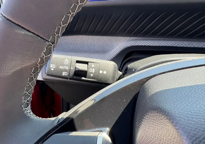 Gros plan sur la commande d'éclairage et clignotants à gauche du volant d'une Citroën C3 rouge Elixir toit noir.