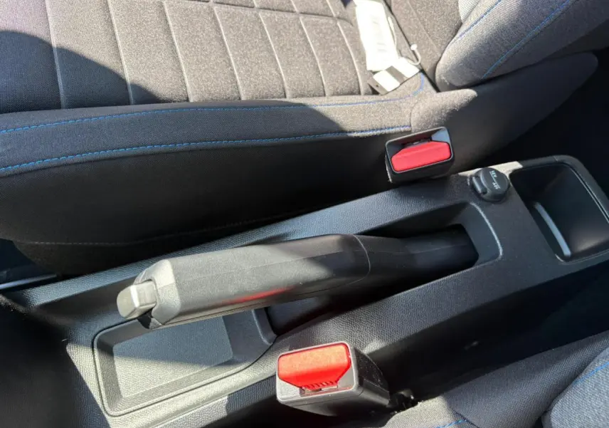 Gros plan sur le frein à main manuel et les ceintures de sécurité rouges entre les sièges avant gris à surpiqûres bleues d'une Citroën C3 2025.