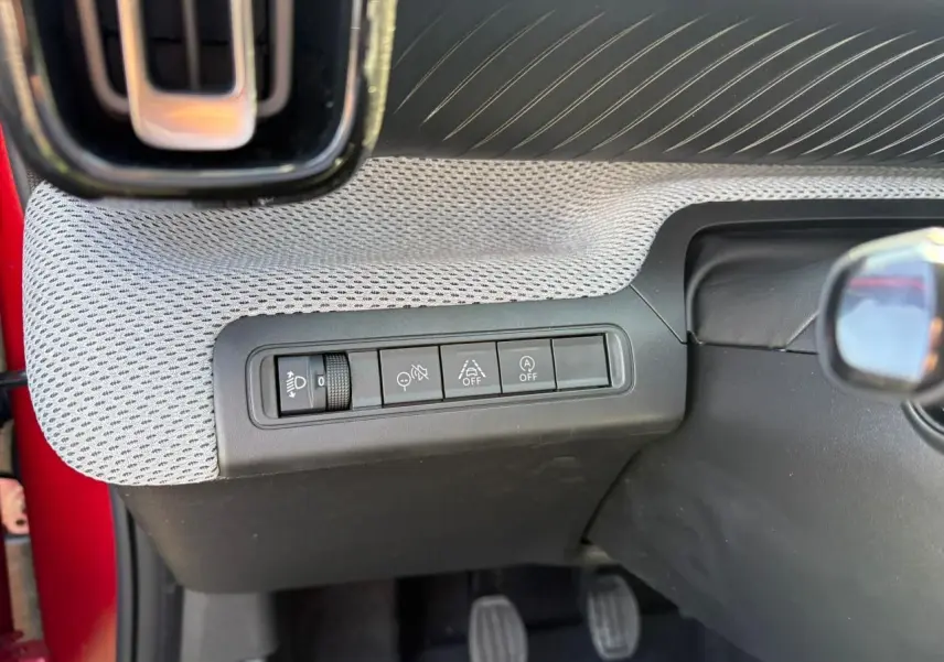 Vue rapprochée des commandes d'assistance au conducteur sur la planche de bord grise d'une Citroën C3 rouge Elixir toit noir.