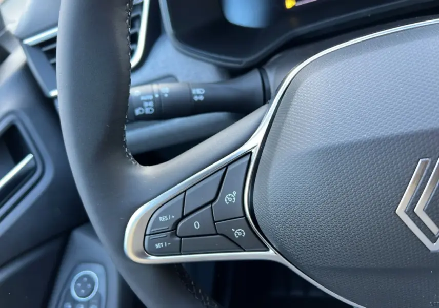 Gros plan sur le volant noir de la Renault Clio 2025 avec commandes intégrées et logo chromé au centre.