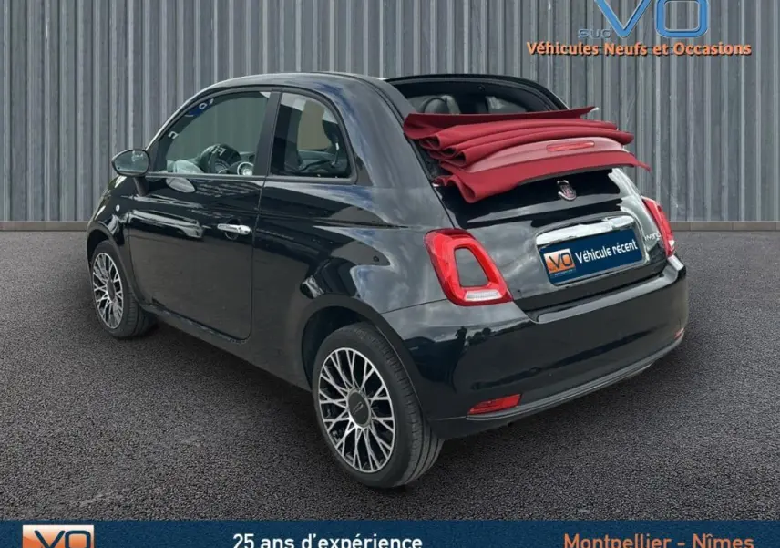 Vue 3/4 arrière droite d'une FIAT 500C noire 2024 avec toit ouvrant rouge replié et roue de secours visible