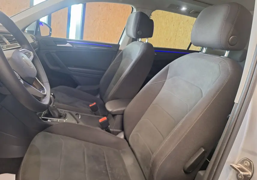 Vue intérieure côté conducteur du Volkswagen Tiguan 2021, sièges microfleece gris avec éclairage d'ambiance bleu sur la portière.