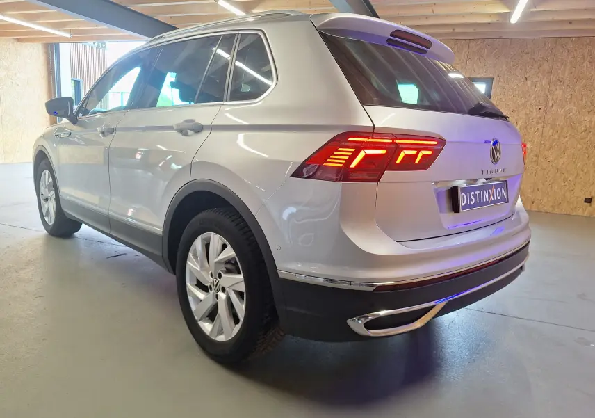 Vue 3/4 arrière droite d'un Volkswagen Tiguan gris métallisé avec feux arrière LED allumés et jantes alliage 18 pouces.