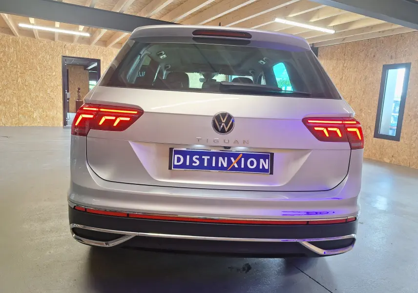 Vue arrière d'un Volkswagen Tiguan gris métallisé avec feux arrière LED allumés dans un intérieur clair.