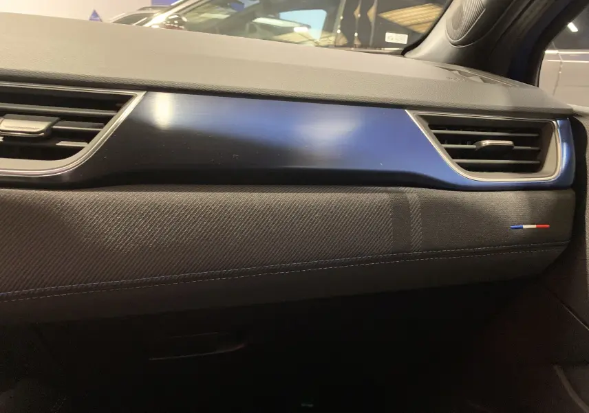 Détail de la planche de bord côté passager du Renault Symbioz bleu Iron avec surpiqûres bleues et drapeau tricolore.