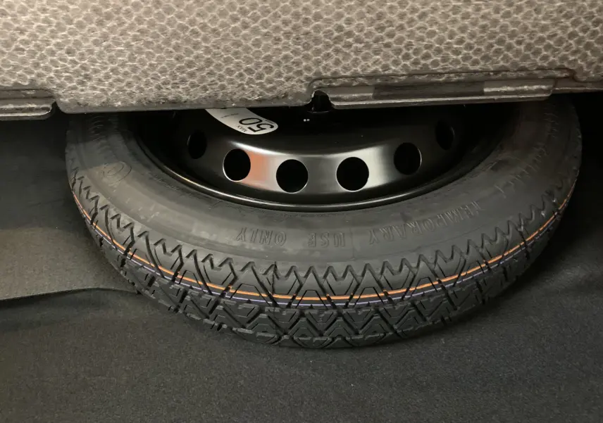 Gros plan sur la roue de secours noire avec pneu marqué "Temporary Use Only" sous le coffre d'une Renault Symbioz Bleu Iron.