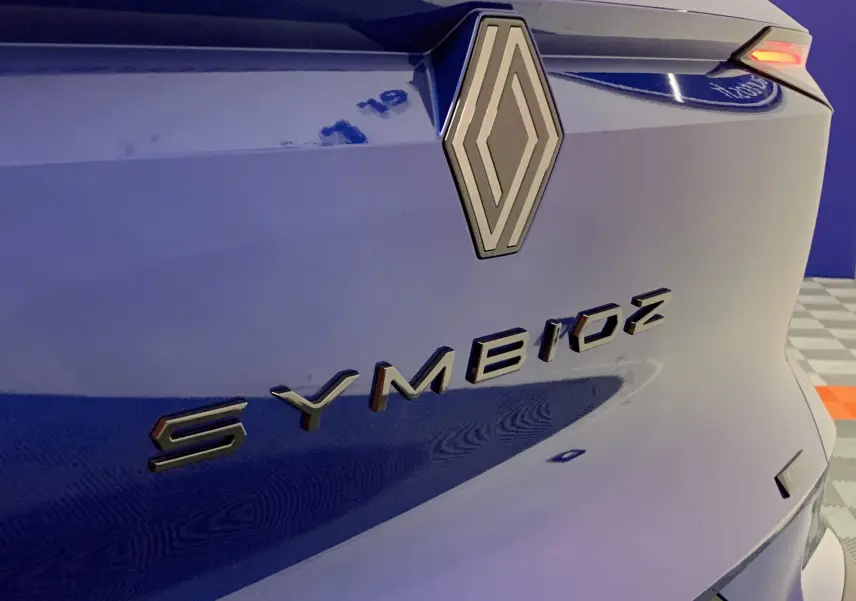 Gros plan sur l'arrière bleu iron du Renault Symbioz avec logo et badge E-TECH visible en angle latéral droit.