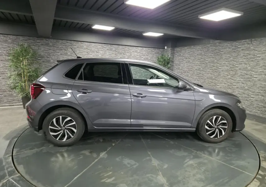 Volkswagen Polo gris métallisé vue de profil côté gauche dans un showroom avec jantes alliage noires et chromées.