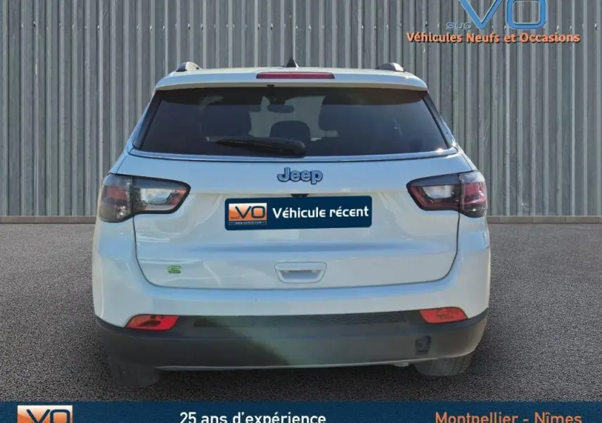 Vue arrière d'un Jeep Compass blanc 2023 avec feux arrière fumés et barres de toit visibles sur fond neutre.