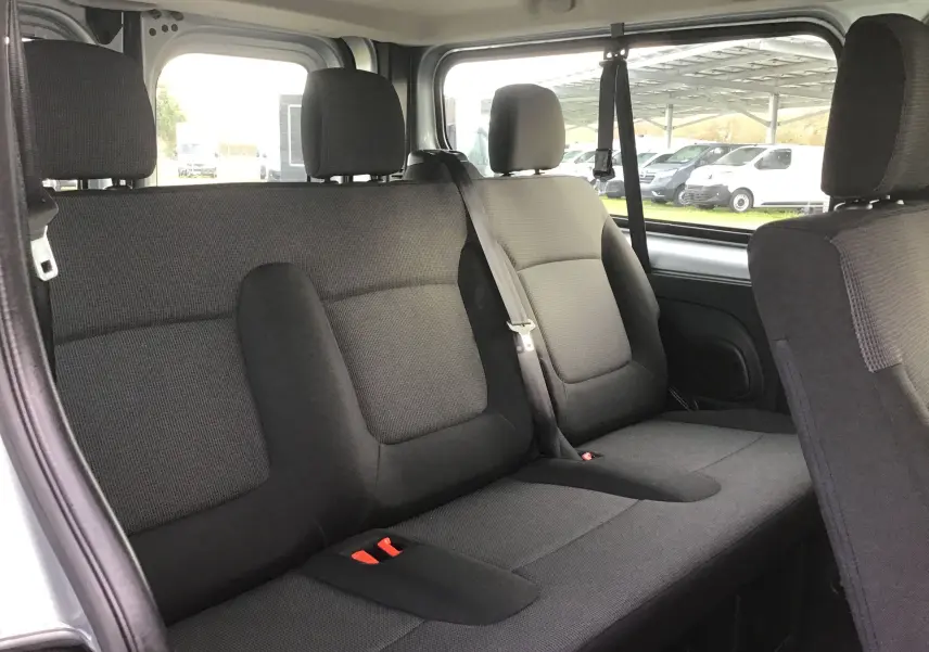 Vue intérieure côté droit montrant la banquette arrière noire du Renault Trafic Combi L2 gris clair 2023, avec ceintures et appuie-têtes.