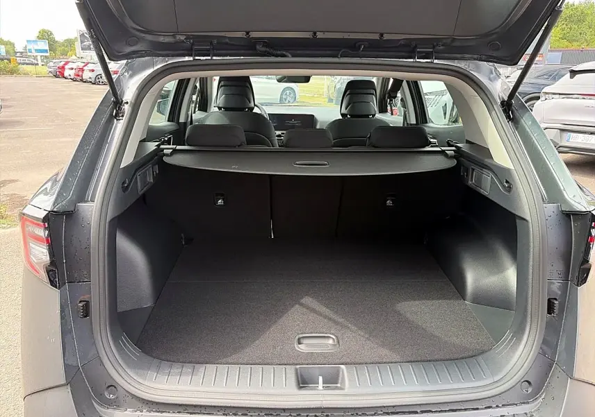 Coffre ouvert vu de l’arrière d’un KIA Sportage gris eclipse 2026 avec cache-bagages et banquette rabattue.