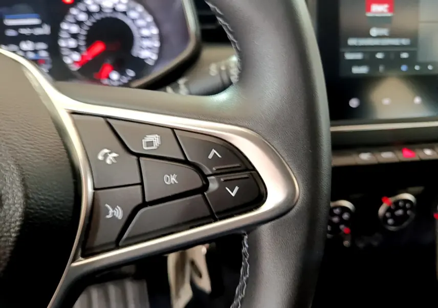 Gros plan sur les commandes du volant côté gauche d'une Renault Clio Business blanche de 2021, tableau de bord flou en arrière-plan.