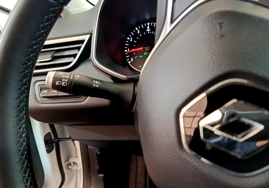 Vue rapprochée du volant cuir et du tableau de bord d'une Renault Clio Business blanche, avec commandes lumineuses visibles.