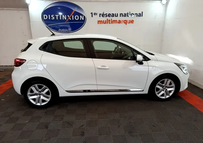 Profil droit d'une Renault Clio Business blanche 2021 dans un showroom avec logo Distinxion en arrière-plan.