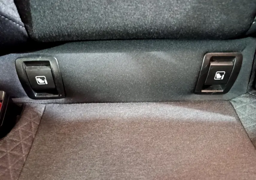 Gros plan sur les commandes de rabattement des sièges arrière en tissu gris de la Renault Clio Business blanche.