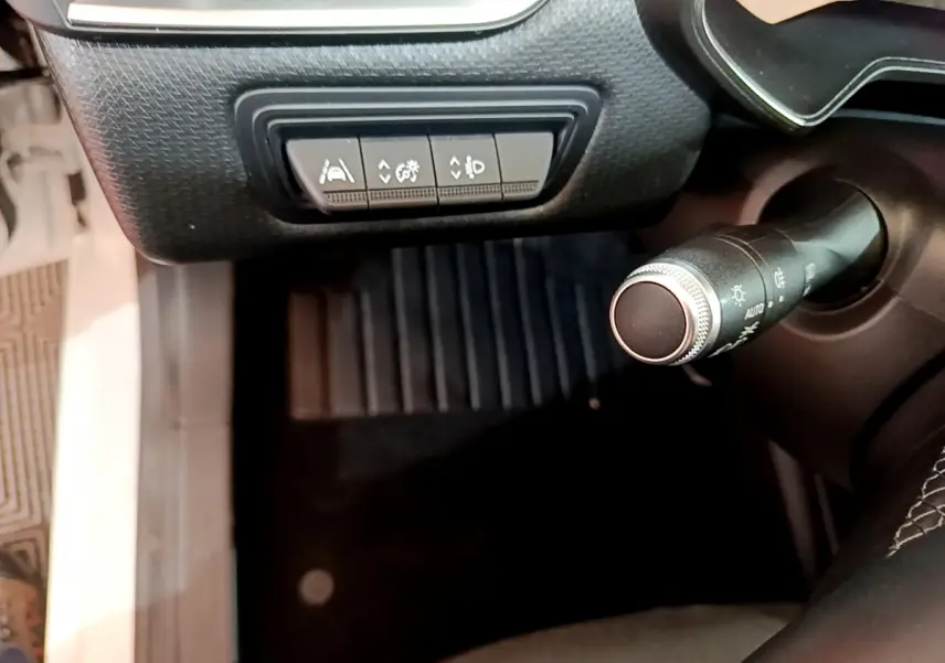 Gros plan sur les commandes d'assistance et la manette d'éclairage côté gauche dans l'habitacle d'une Renault Clio Business blanche.