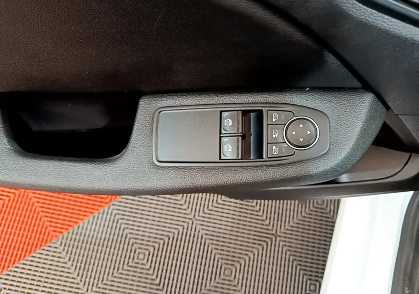 Gros plan sur la commande des vitres et rétroviseurs côté conducteur d'une Renault Clio Business blanche, intérieur noir.