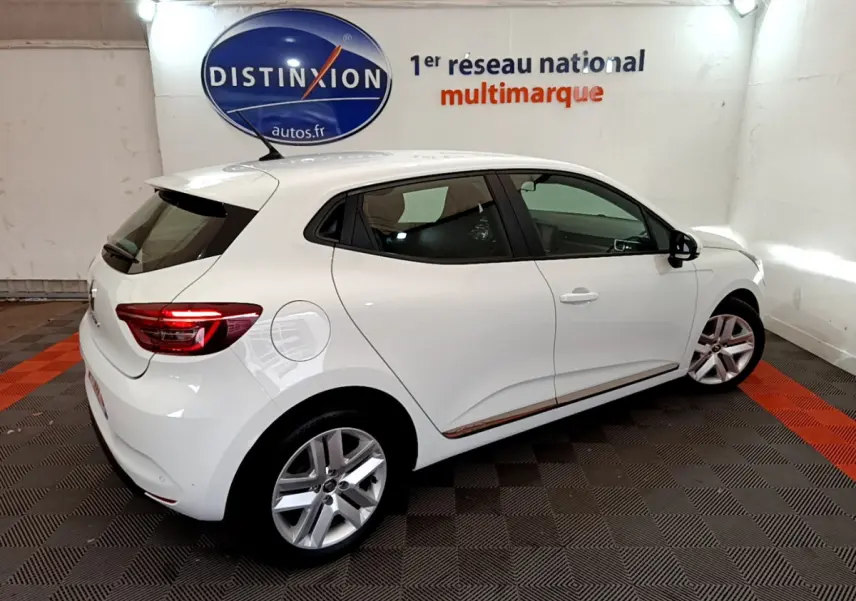 Vue 3/4 arrière droite d'une Renault Clio Business blanche, avec jantes alliage et feux arrière LED visibles en intérieur showroom.