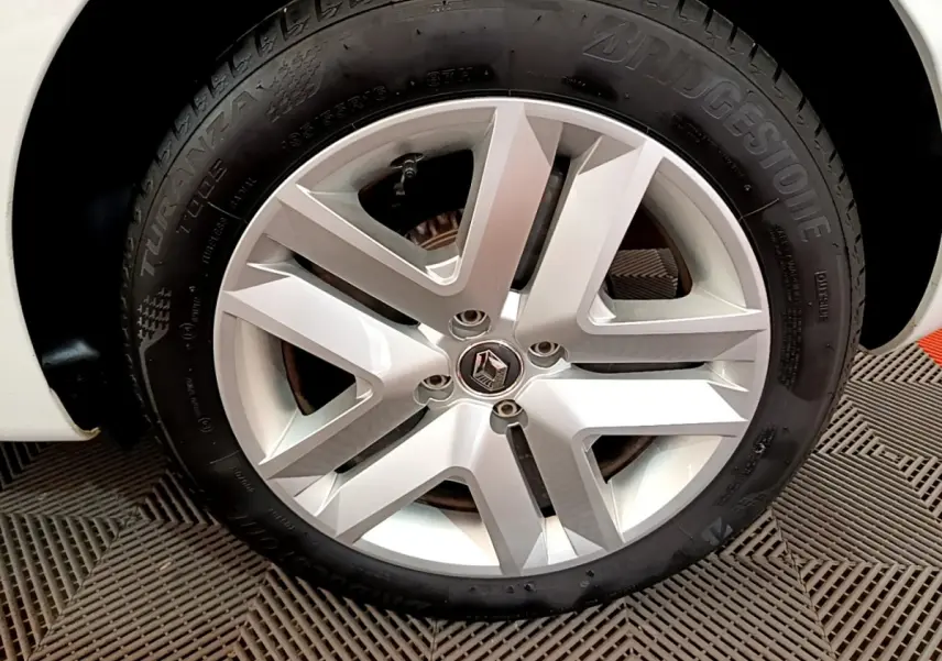 Gros plan sur la roue arrière droite blanche d'une Renault Clio Business SCe 65 de 2021, sur sol texturé.