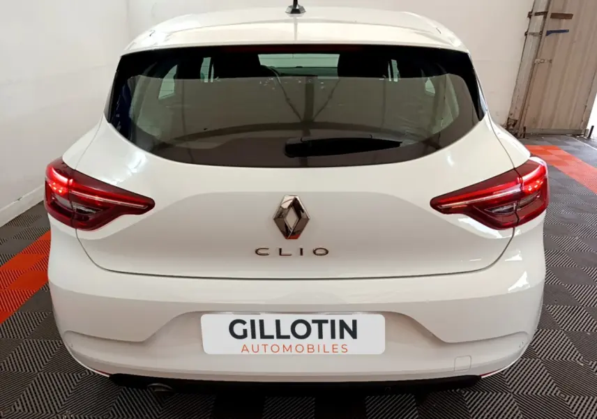 Vue arrière d'une Renault Clio blanche 2021 avec feux LED et logo Renault bien visibles sur fond intérieur showroom.