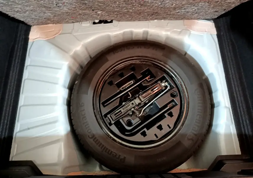 Gros plan sur la roue de secours noire et les outils de bord dans le coffre blanc d'une Renault Clio Business 2021.