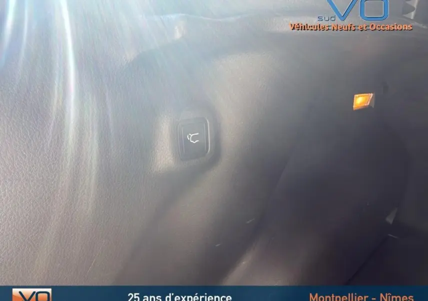 Détail intérieur du coffre du Jeep Compass gris 2023, bouton d'ouverture électrique de hayon visible sur la paroi.