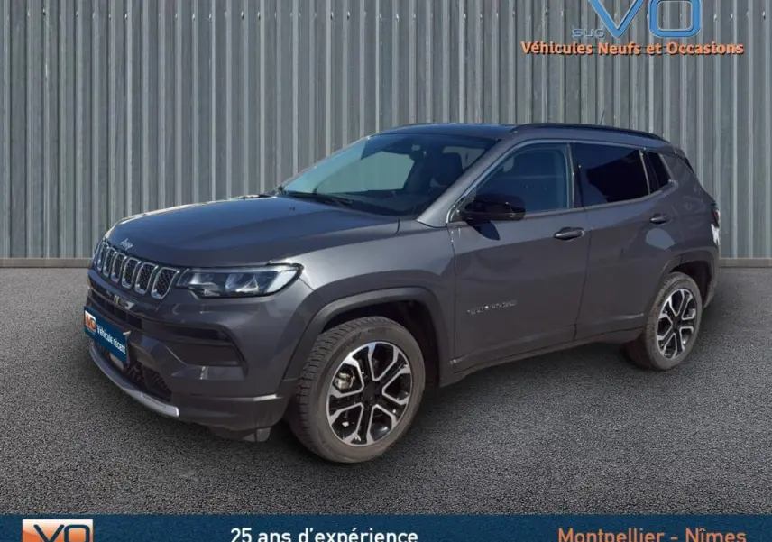 Jeep Compass gris en 3/4 avant droit, avec jantes 18 pouces et barres de toit visibles sur fond urbain.