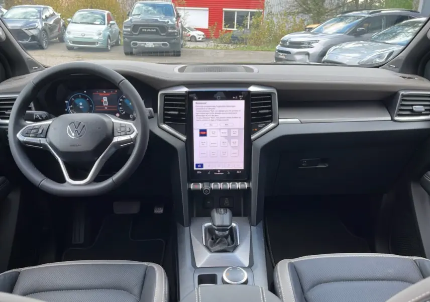 Vue intérieure du tableau de bord du Volkswagen Amarok noir, avec écran tactile vertical et volant multifonctions cuir.