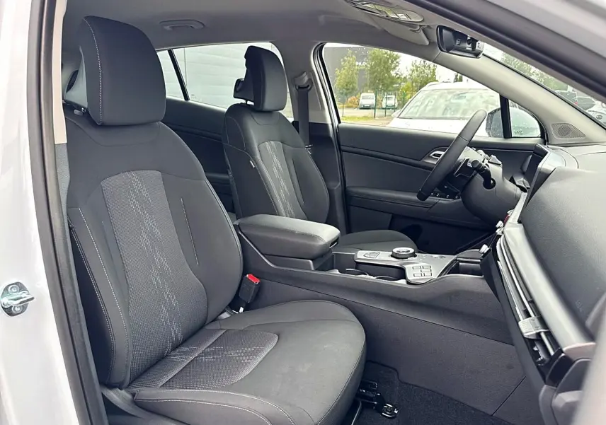 Intérieur du Kia Sportage 1.6 hybride blanc, vue côté gauche sur sièges avant et console centrale avec accoudoir.