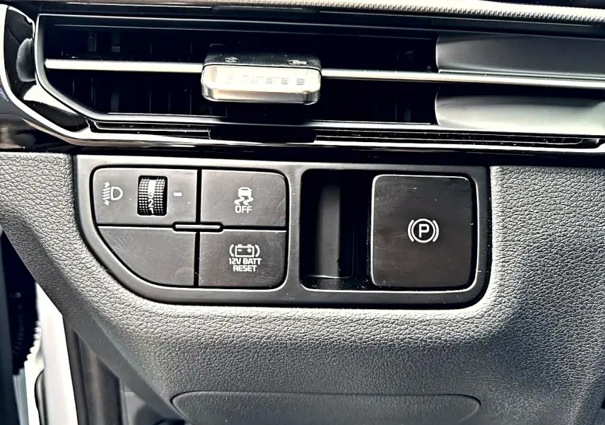 Vue rapprochée des commandes noires du tableau de bord du Kia Sportage blanc, avec bouton frein à main électronique.