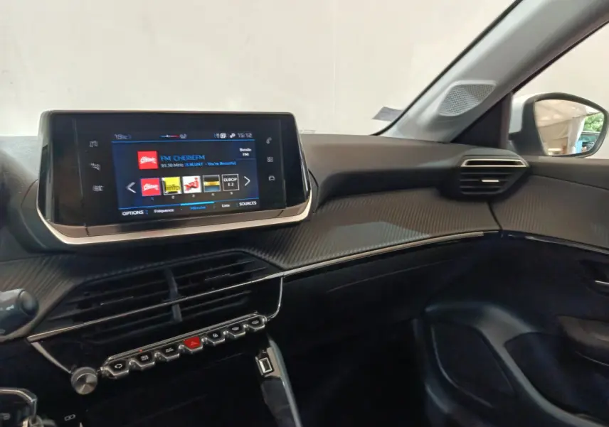 Vue intérieure côté passager du tableau de bord noir de la Peugeot 208 PureTech 100 avec écran tactile multimédia allumé.