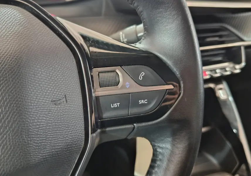 Gros plan sur les commandes gauche du volant cuir noir du Peugeot 208 blanc, avec boutons de téléphone et audio visibles.