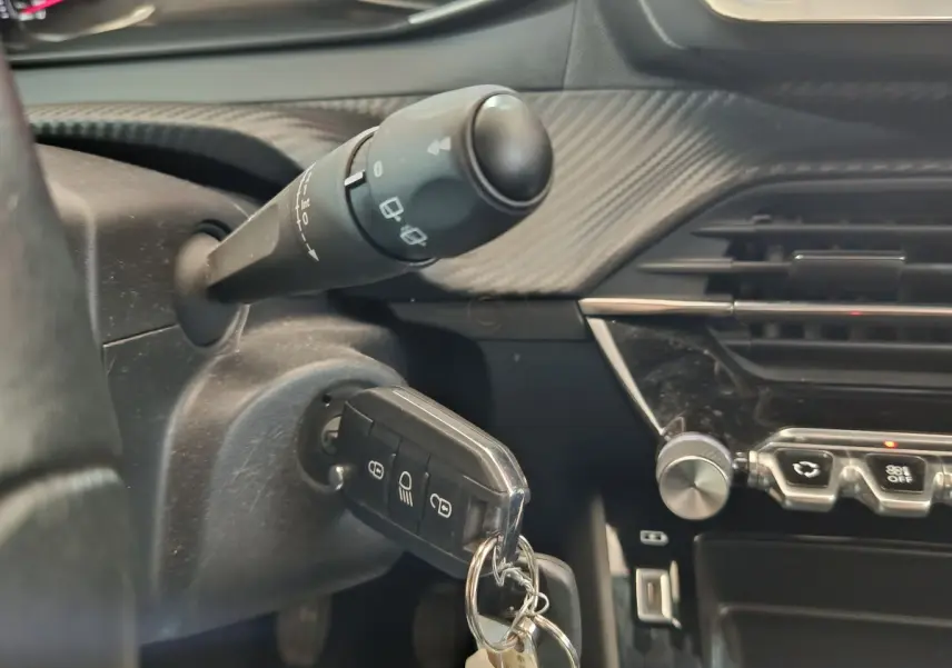 Gros plan intérieur sur le contacteur et la clé de la Peugeot 208 blanche, avec tableau de bord noir et commandes visibles.