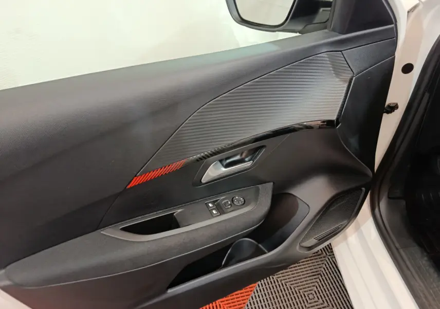 Intérieur côté conducteur de la Peugeot 208 blanche, porte avec insert carbone et bande rouge décorative.