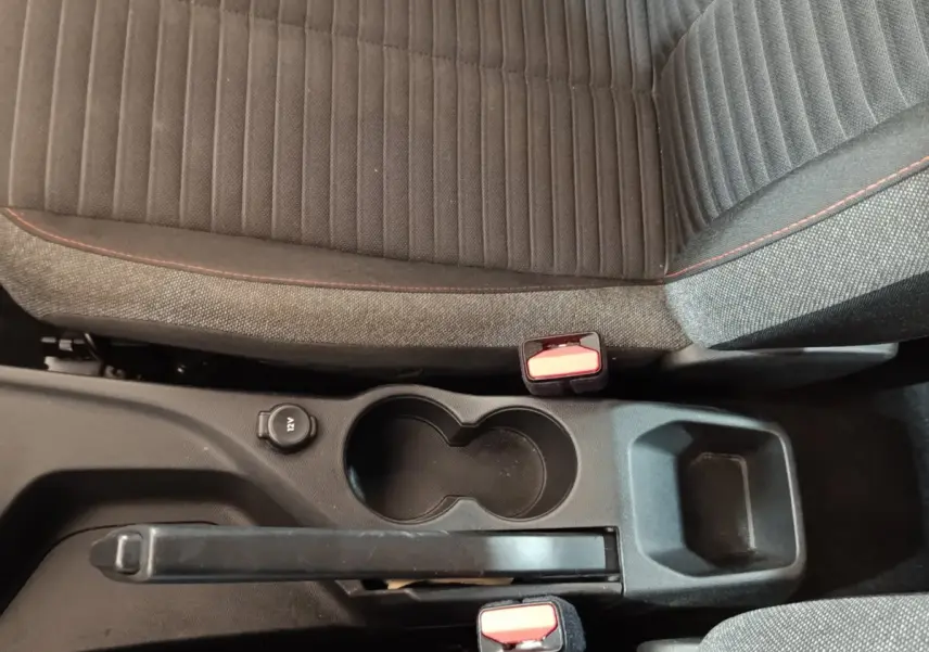 Vue plongeante sur la console centrale noire et les sièges tissu gris foncé avec surpiqûres rouges d'une Peugeot 208 blanche.