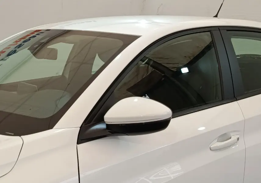 Vue latérale côté gauche d'une Peugeot 208 blanche avec rétroviseur et poignée de porte visibles.