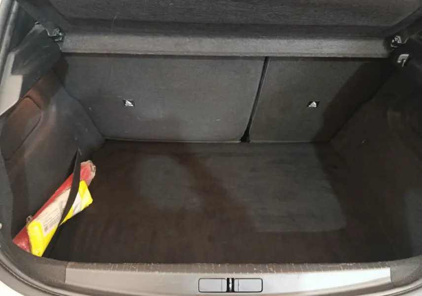 Coffre ouvert d'une Peugeot 208 blanche, vue de dessus, montrant un espace de chargement vide avec un kit de sécurité sur le côté.