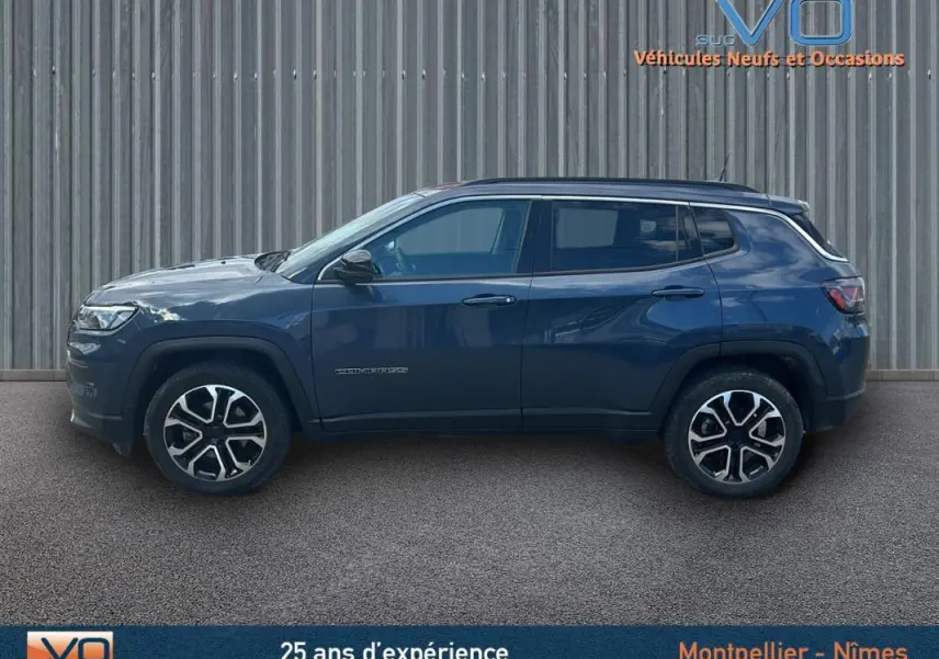 Jeep Compass bleu vue de profil côté gauche, avec jantes 18 pouces et barres de toit visibles sur fond neutre.