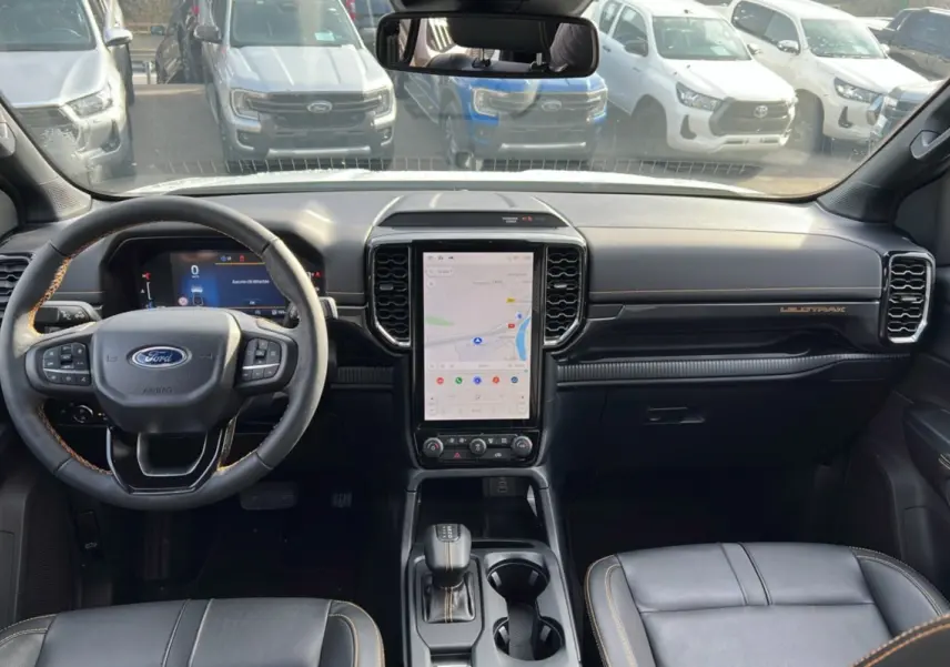 Vue intérieure frontale du Ford Ranger Wildtrak 2025, tableau de bord noir avec écran tactile vertical et volant cuir.