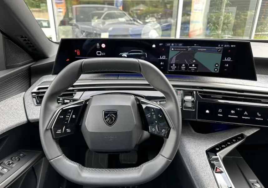 Vue intérieure centrée sur le volant cuir et le tableau de bord numérique panoramique du Peugeot 3008 gris Artense.