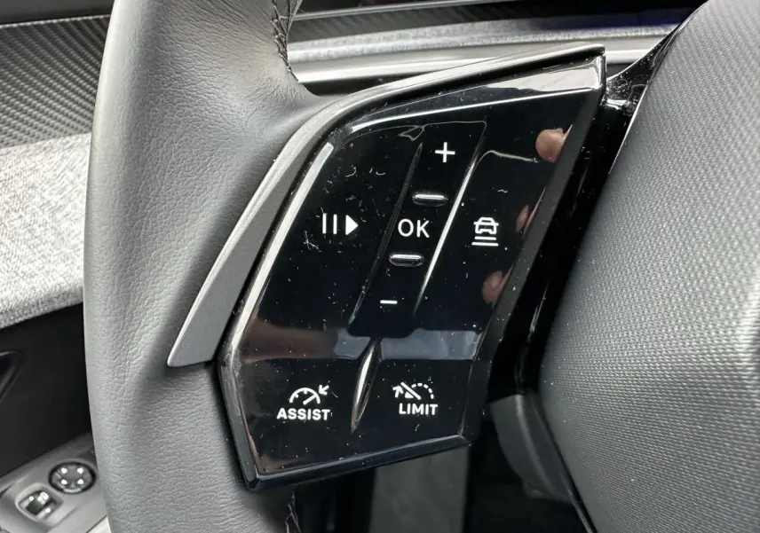 Gros plan sur les commandes au volant gauche du Peugeot 3008 2024, boutons noirs brillants avec fonctions assist et limiteur.