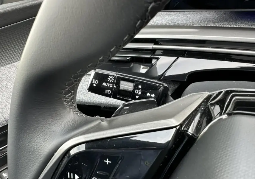 Gros plan sur le volant et la commande des phares du Peugeot 3008 2024, intérieur noir avec finitions brillantes.