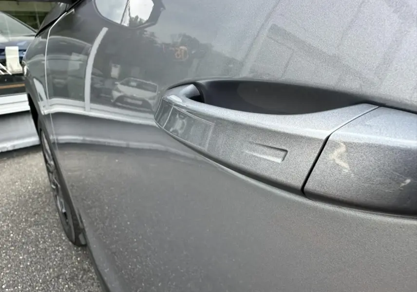 Gros plan sur la poignée de porte côté gauche du Peugeot 3008 gris Artense, reflétant l'environnement extérieur.