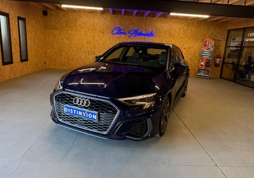 Audi A3 2.0 TDI S-Line bleu vue 3/4 avant droit dans un showroom avec mur en bois et enseigne lumineuse.