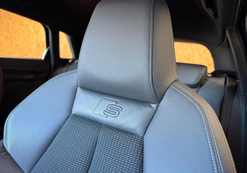Gros plan sur le siège avant en cuir noir de l'Audi A3 S-Line avec logo "S" embossé, intérieur visible en arrière-plan.