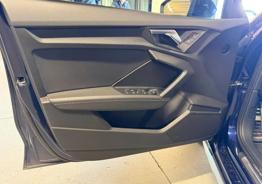 Vue rapprochée de la porte avant gauche bleu foncé d’une Audi A3 2.0 TDI S-Line avec commandes de vitres et poignée argentée.
