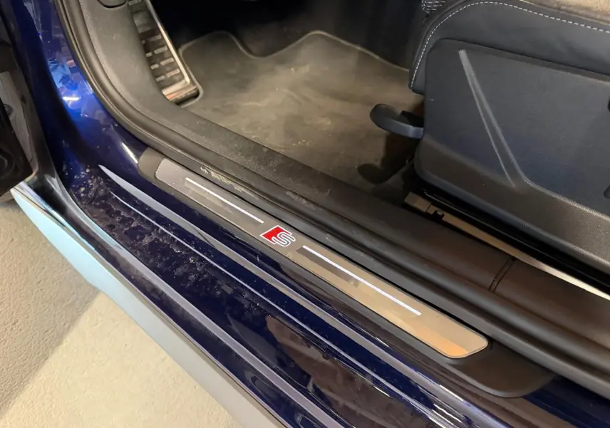 Gros plan sur la porte côté conducteur d’une Audi A3 bleu 2022 avec seuil de porte S-Line et intérieur noir.